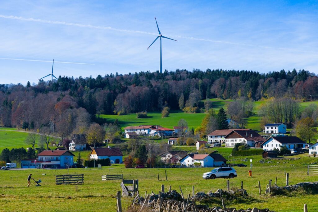 Gratuit Village pittoresque des Breuleux avec des éoliennes modernes et des champs verdoyants sous un ciel bleu clair. Photos